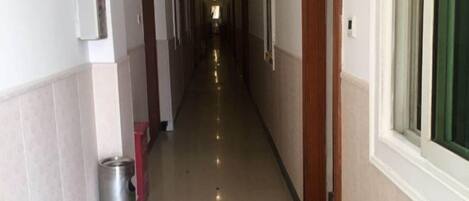 A long, narrow hallway with doors on both sides, a trash bin, and a window on the right.