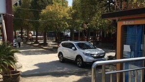 A street view with a white SUV parked on the side, trees lining the road, and a building with a sign that reads "香花社区". - Yongshun Hotel (Shanghai)