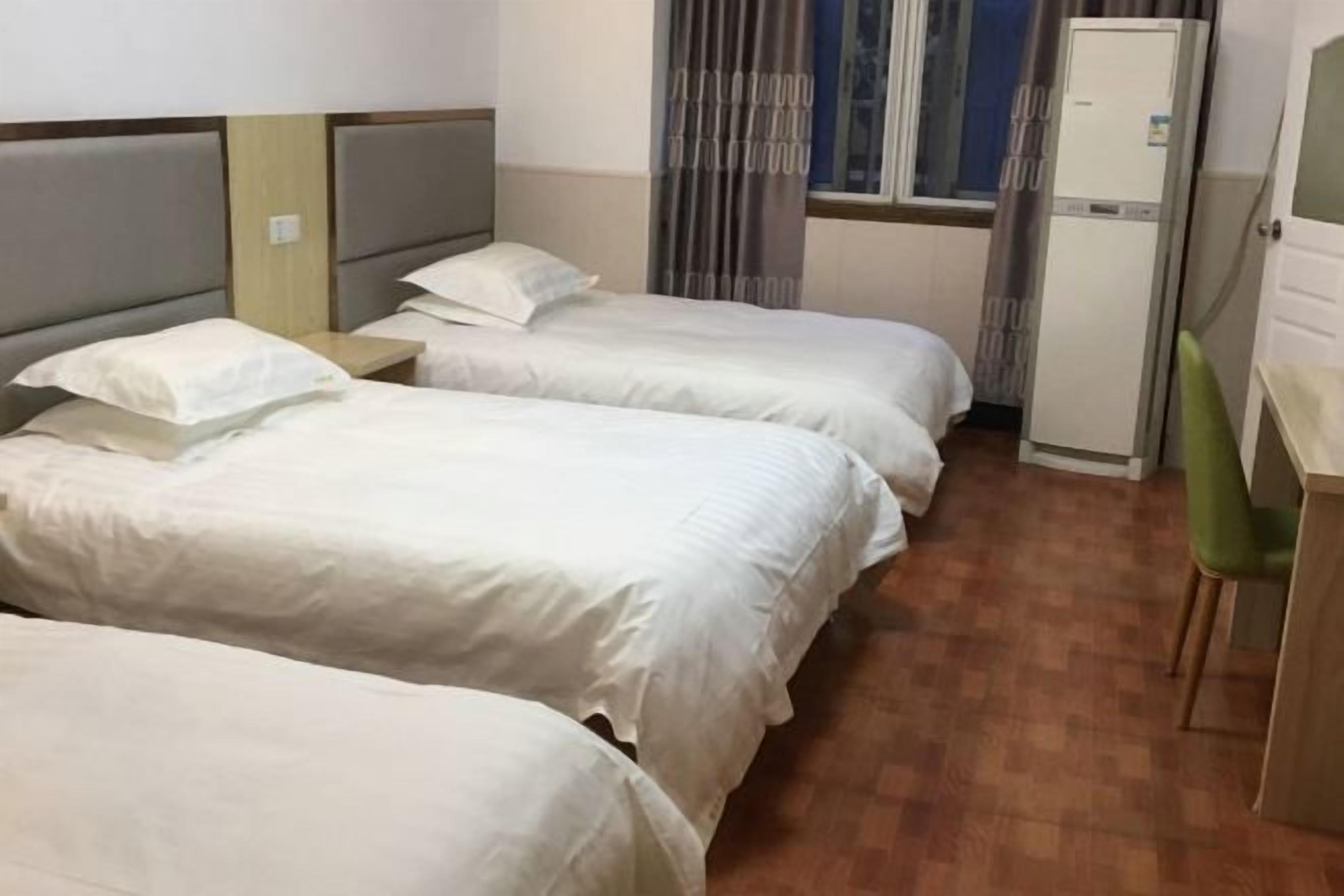 Een hotelkamer met drie bedden, een bureau, een stoel en een raam met gordijnen.