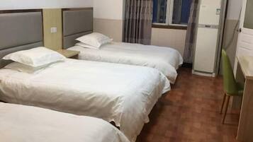 Een hotelkamer met drie bedden, een bureau, een stoel en een raam met gordijnen.