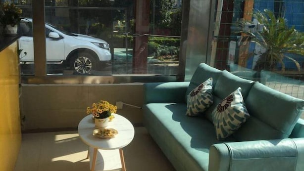 A room with a teal sofa, a small round table with a vase of flowers, and a view of a white car through a window. - Yongshun Hotel (Shanghai)