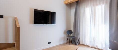 Una sala de estar moderna con una escalera de madera, un televisor de pantalla plana montado en la pared, un sofá gris, una mesita y una silla.
