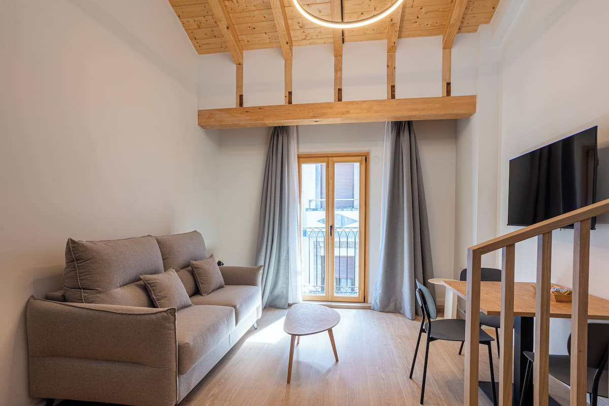 A modern living room with a wooden ceiling, a sofa, a small table, and a TV mounted on the wall.