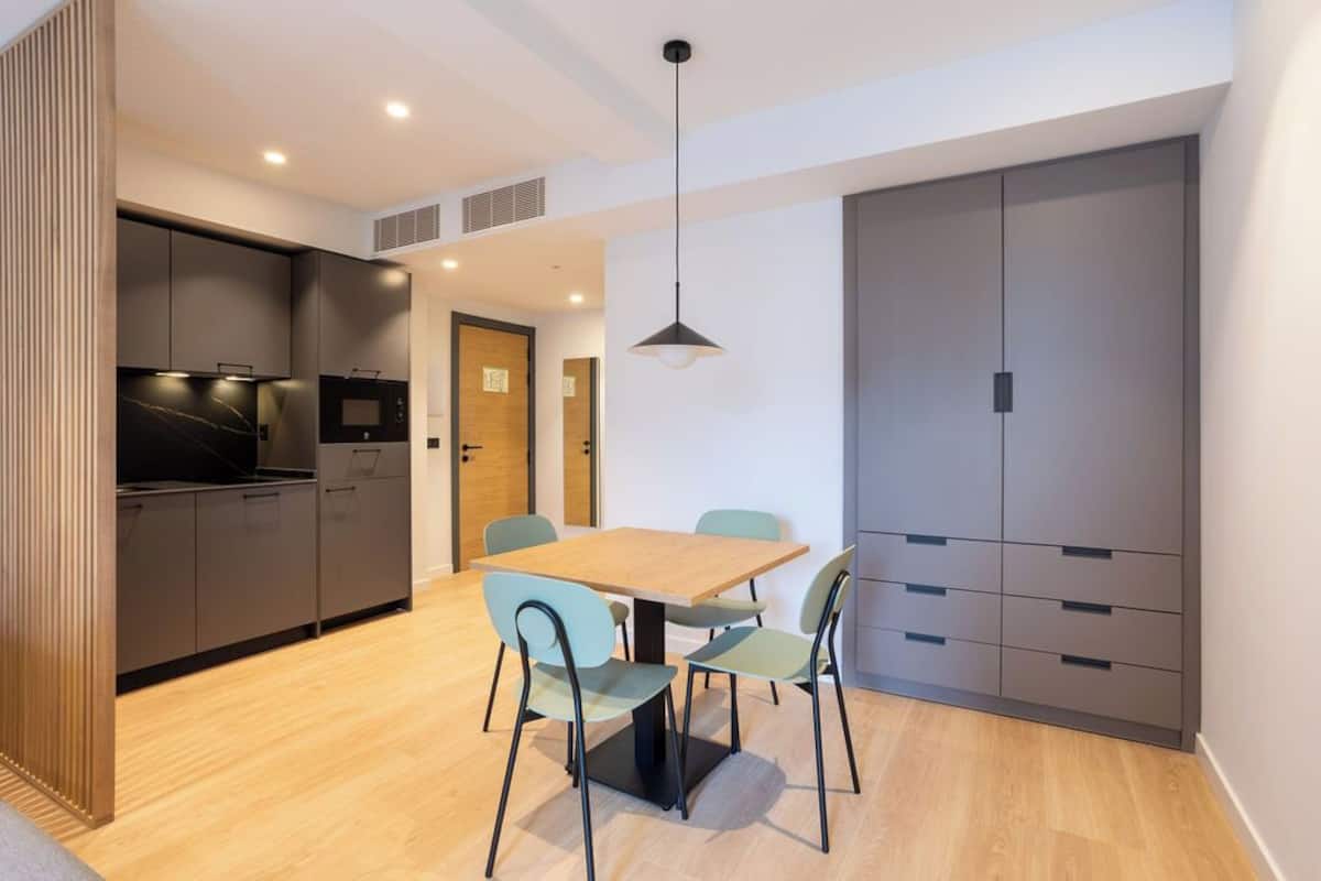 A modern kitchen with dark cabinets, a wooden dining table, and light-colored chairs.