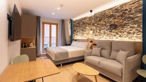 A modern hotel room with a stone accent wall, a bed, a sofa, a dining table, and a TV. - Be10 Suites (Bermeo)