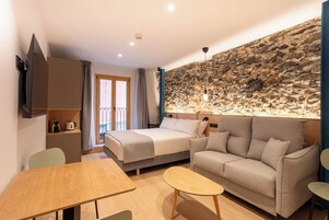 Una habitación de hotel moderna con una pared de acento de piedra, una cama, un sofá, una mesa de comedor y un televisor.