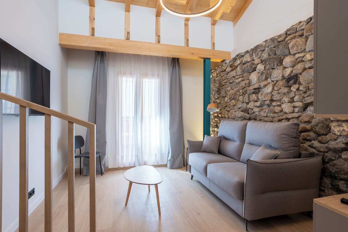 A modern living room with a stone wall, a wooden ceiling, and a grey sofa.