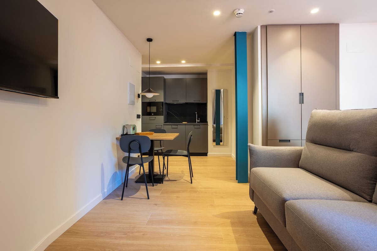 A modern living room with a sofa, a dining area with a table and chairs, and a kitchen in the background.