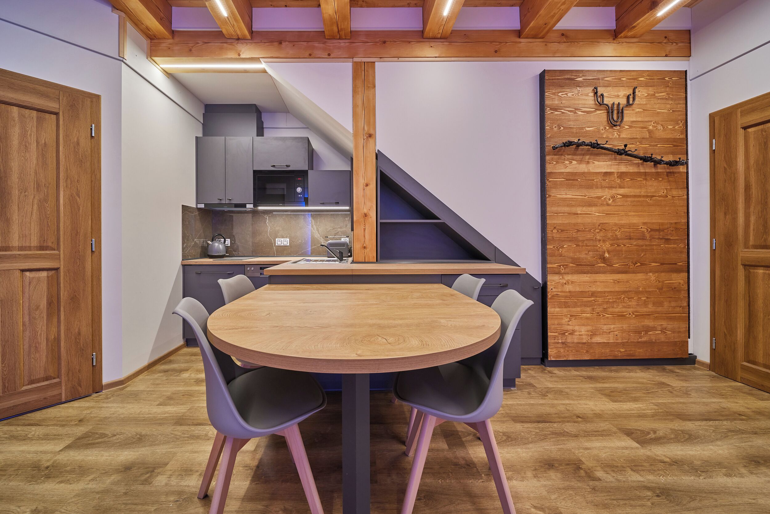 Une cuisine compacte dotée d’appareils électroménagers modernes, un coin repas avec une table et des chaises en bois, et un escalier menant à un niveau supérieur.
