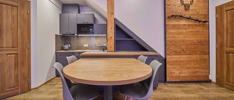 Une cuisine compacte dotée d’appareils électroménagers modernes, un coin repas avec une table et des chaises en bois, et un escalier menant à un niveau supérieur.