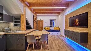 A modern kitchen with a wooden ceiling, a dining area with chairs, a TV mounted on the wall, and a blue-lit pathway. - Sunny, stylish studio in the mountains (Královéhradecký kraj)
