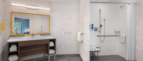 A modern bathroom with a vanity, towel rack, shower, and a mirror with a geometric pattern on the wall.