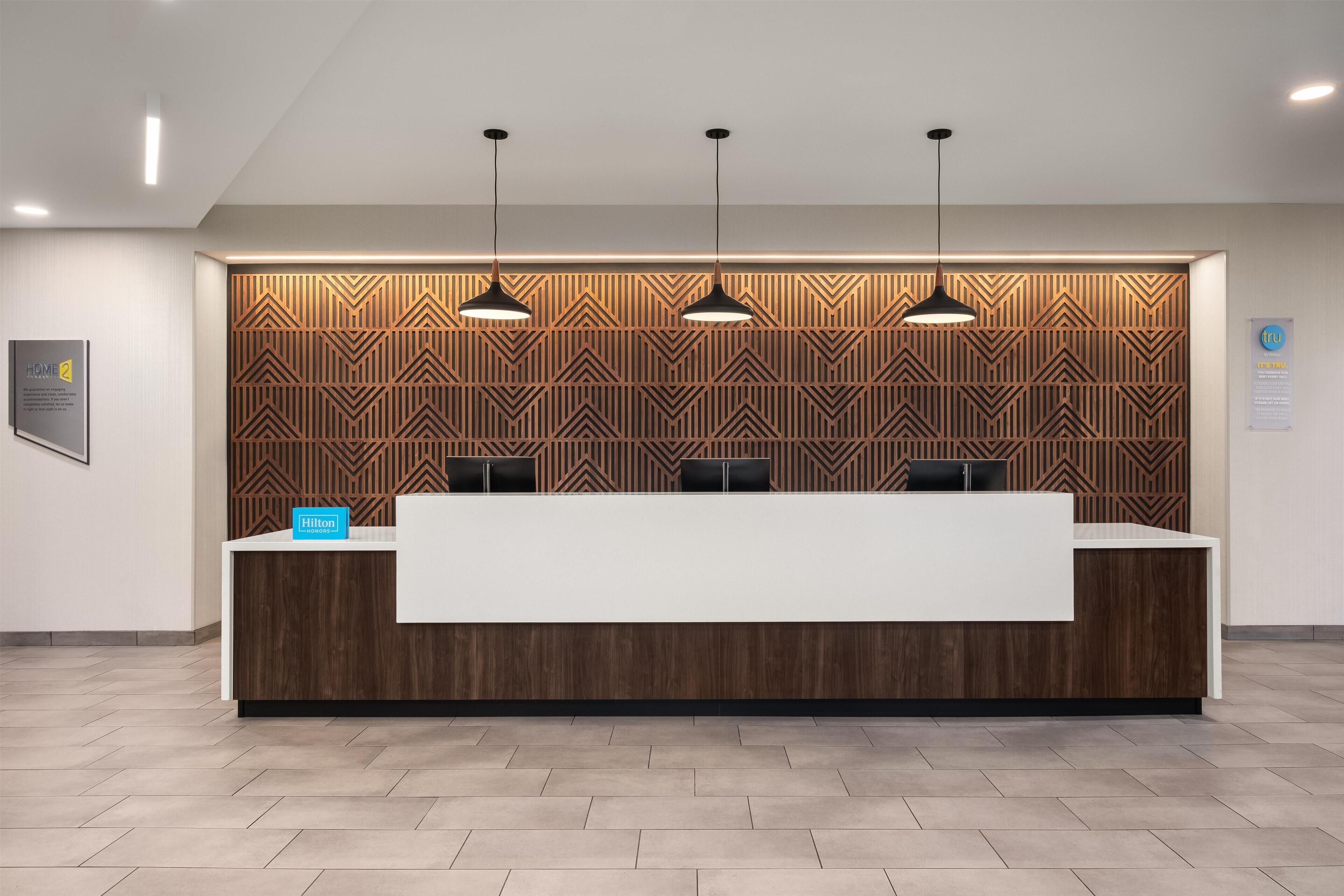 A hotel reception desk with a modern design, featuring a wooden panel wall and three pendant lights.
