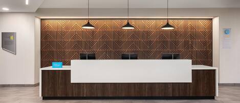 A hotel reception desk with a modern design, featuring a wooden panel wall and three pendant lights.