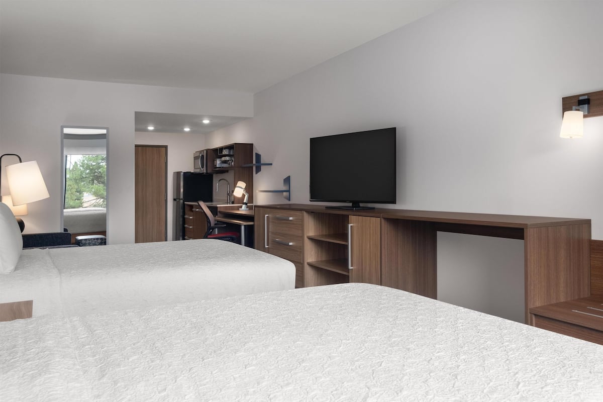 A modern hotel room with two beds, a desk, a TV, and a wardrobe.