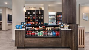 Um saguão de hotel com um balcão central exibindo lanches, bebidas e uma geladeira.