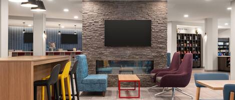 A modern lounge area with a stone wall, a flat-screen TV, and a bar with stools.