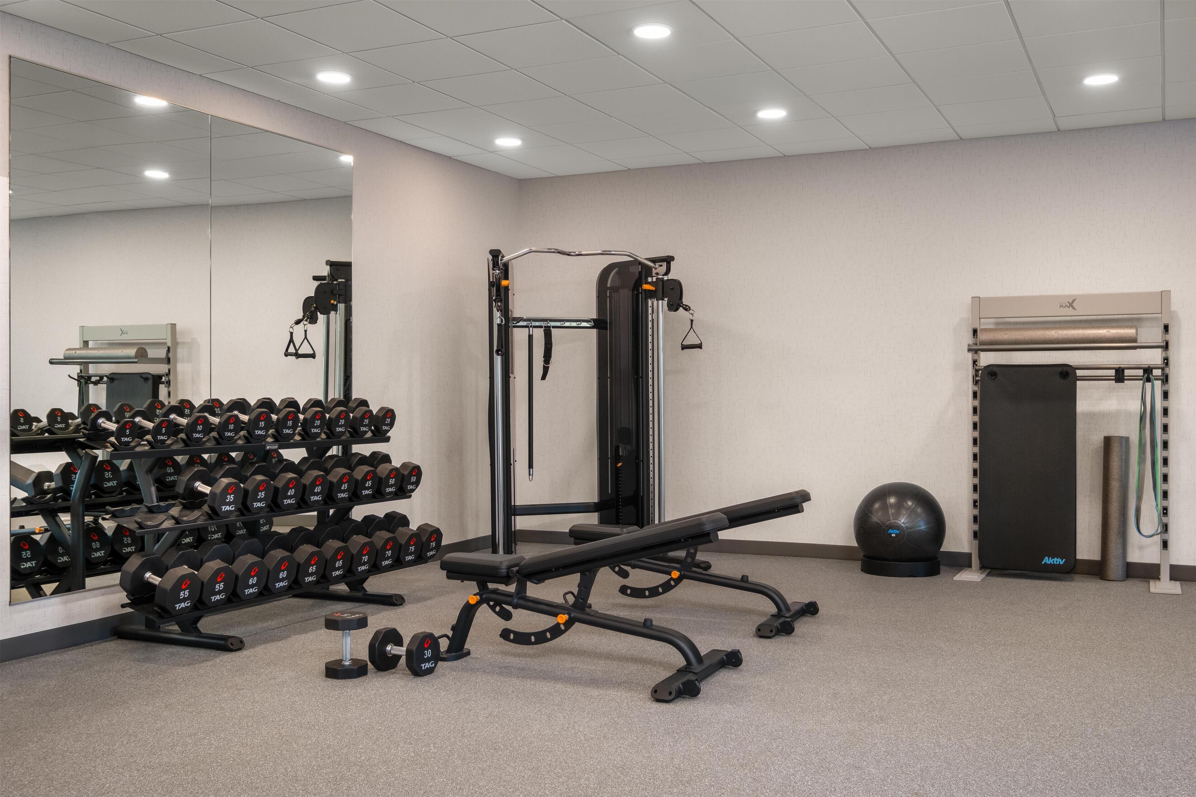 Ett gym med utrustning för styrketräning, en bänk och en vägg med speglar.