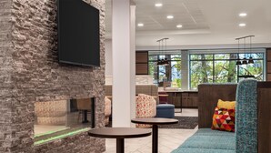Uma área de estar moderna com parede de pedra, televisão de tela plana, mesas redondas e um sofá azul com almofadas coloridas.