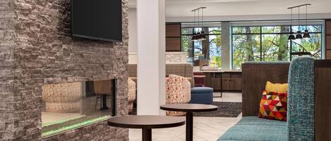 A modern lounge area with a stone wall, a flat-screen TV, round tables, and a blue sofa with colorful cushions.