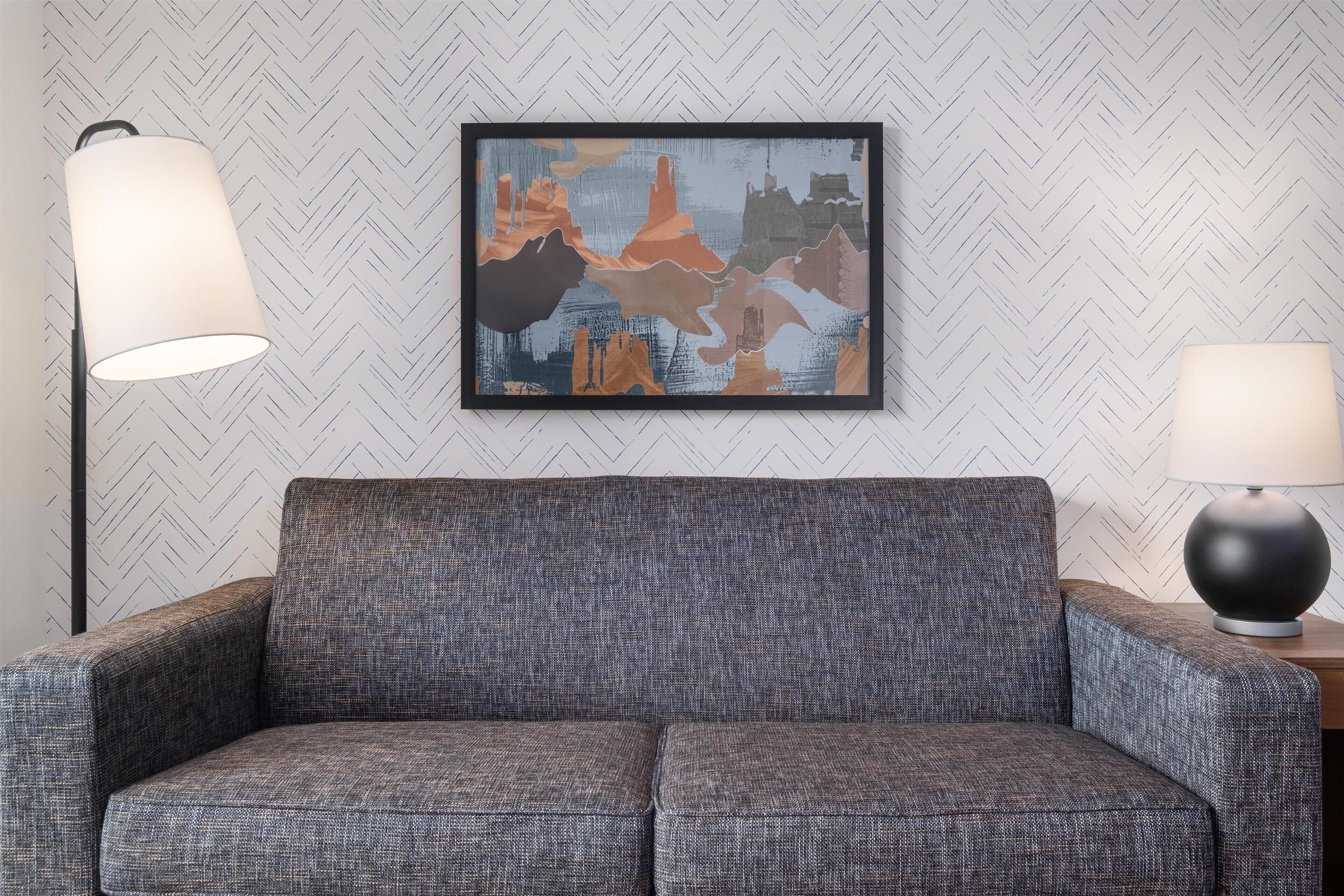 Un sofá tapizado en gris con papel de pared de diseño en patrón de espiga.