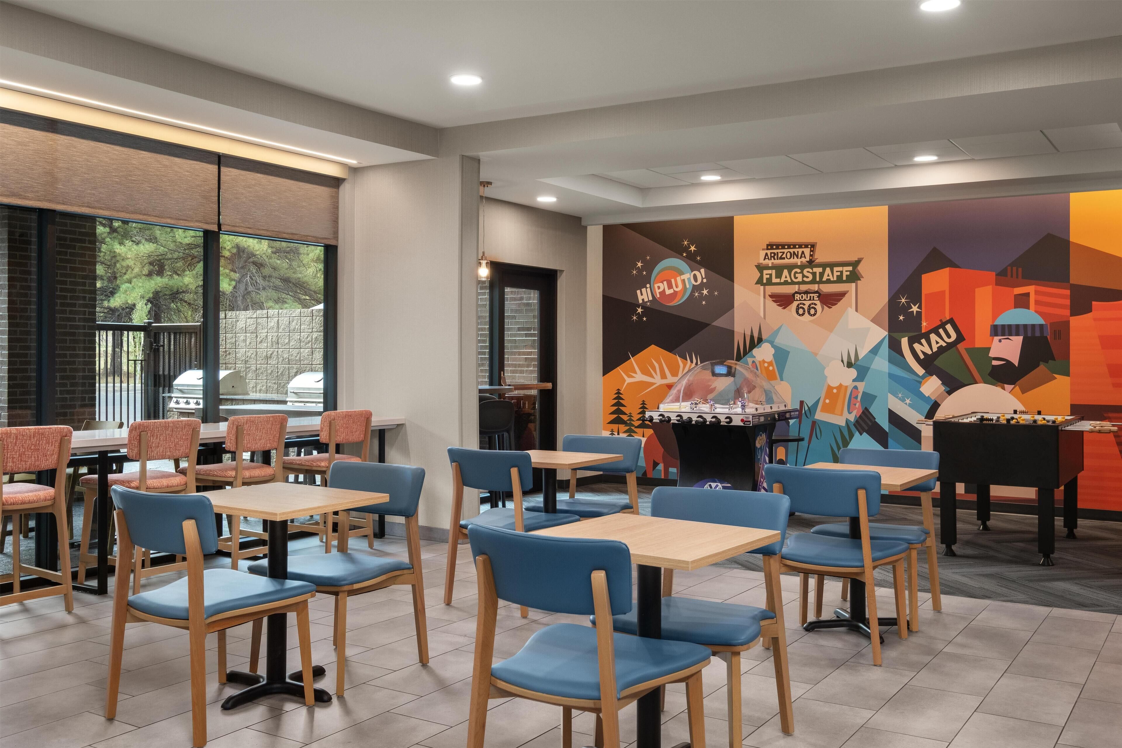 A restaurant with tables and chairs, a foosball table, and a mural on the wall.