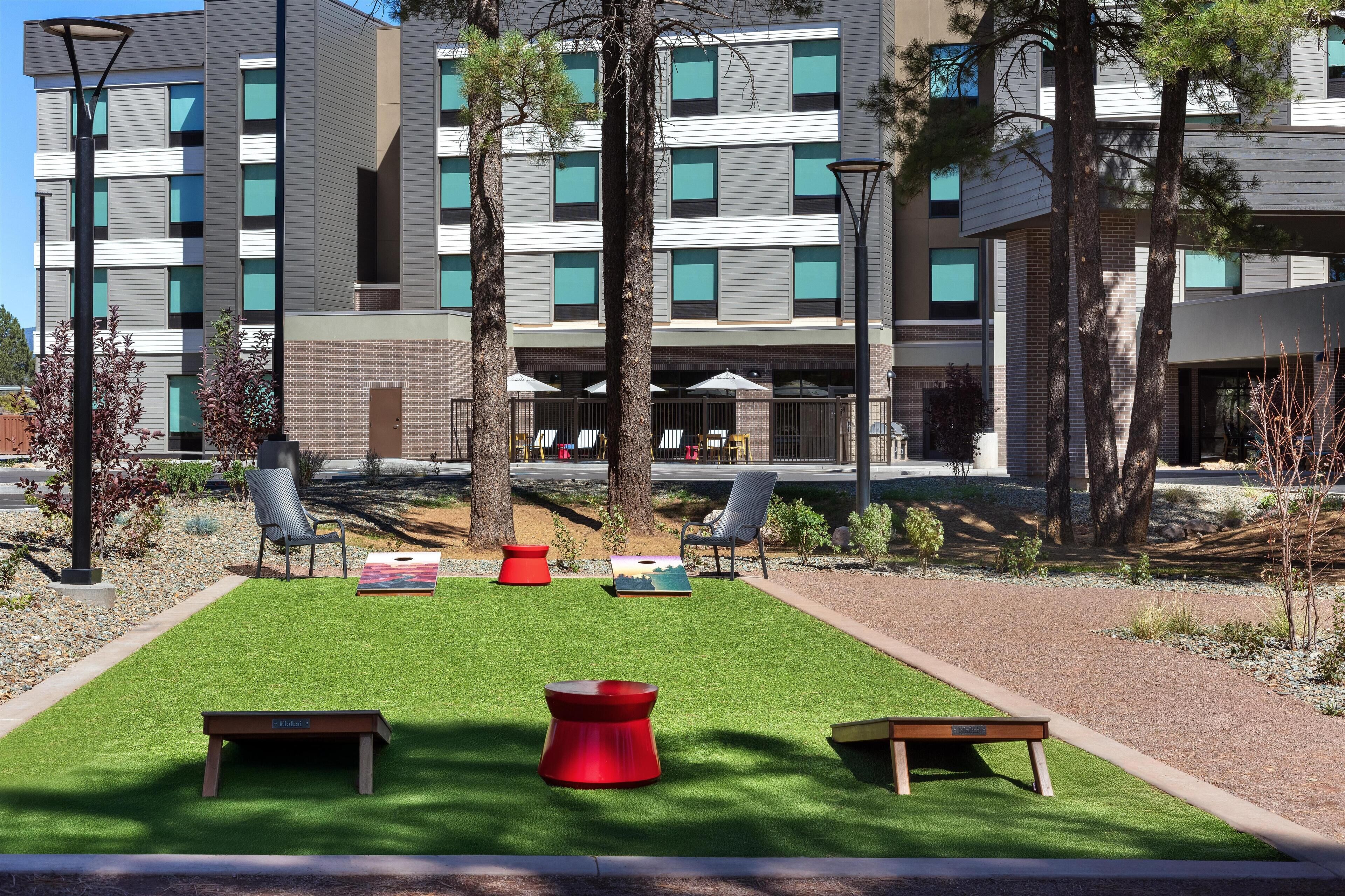 A modern building with multiple floors, outdoor seating area with chairs and tables, and a well-maintained lawn.