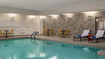 A swimming pool with clear water, surrounded by yellow chairs and tables, and a tiled wall.