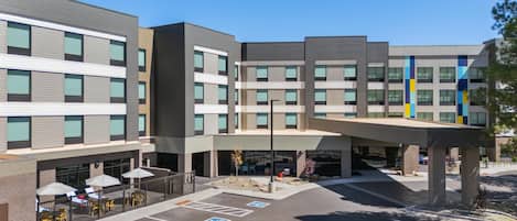 A multi-story hotel with a covered outdoor area, parking, and a landscaped entrance.