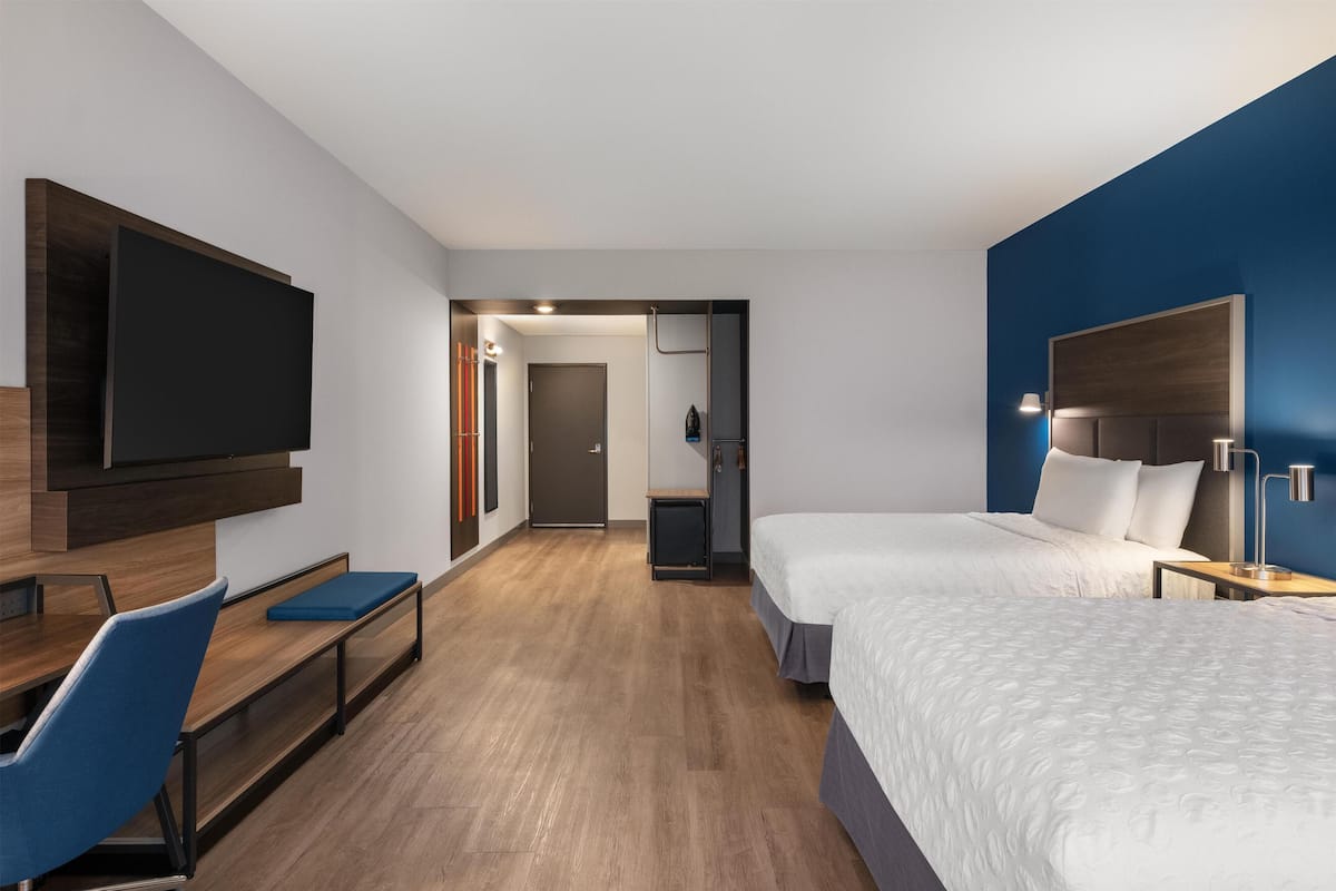 A modern hotel room with a large bed, a desk with a chair, a television mounted on the wall, and a door leading to a bathroom.