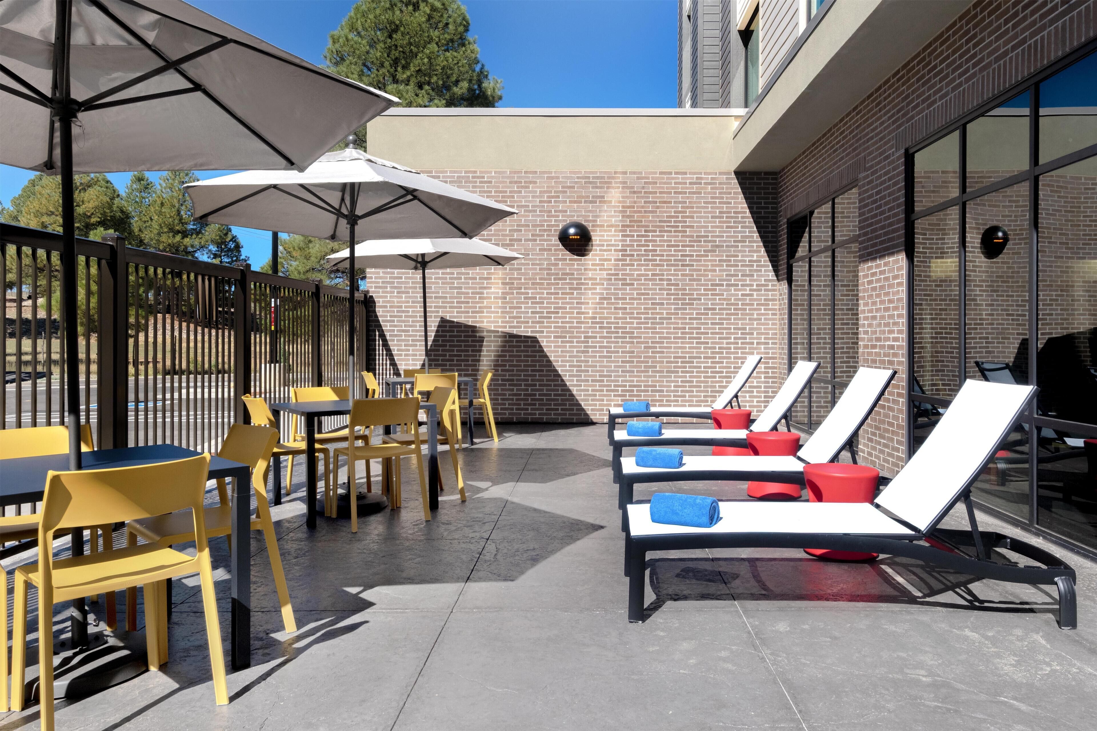An outdoor patio with yellow chairs and tables, sun loungers with towels, and umbrellas.