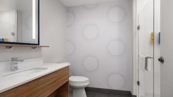 A modern bathroom with a white sink, wooden vanity, a toilet, and a glass shower enclosure.