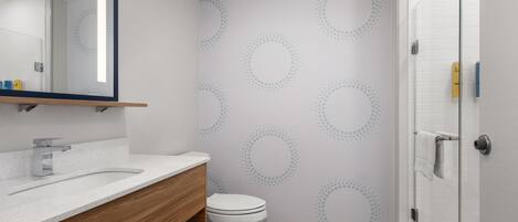 Un baño moderno con un lavamanos blanco, tocador de madera, inodoro y cabina de ducha con mampara de vidrio.