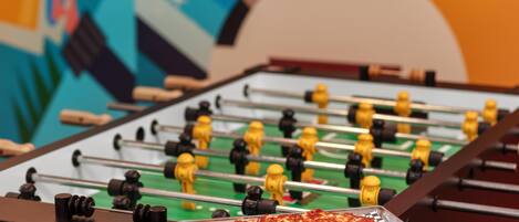 A foosball table with a pizza on a tray in the foreground.