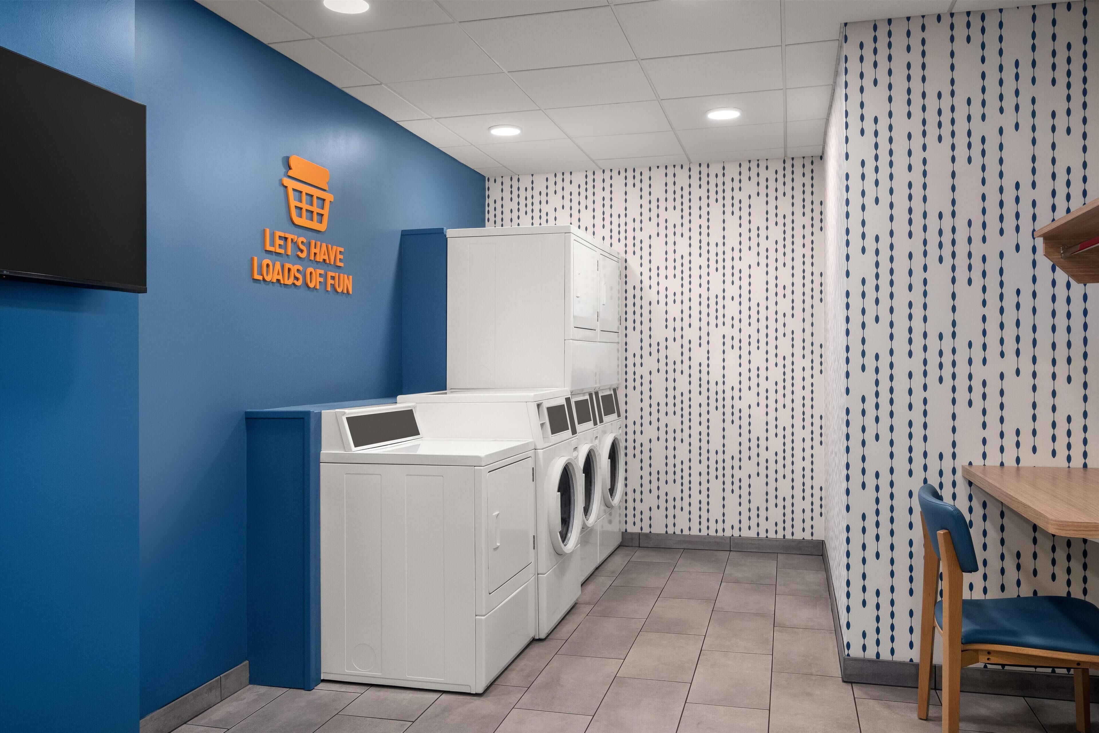 A laundry room with a blue wall, a sign that says "Let's have loads of fun," and a washing machine.