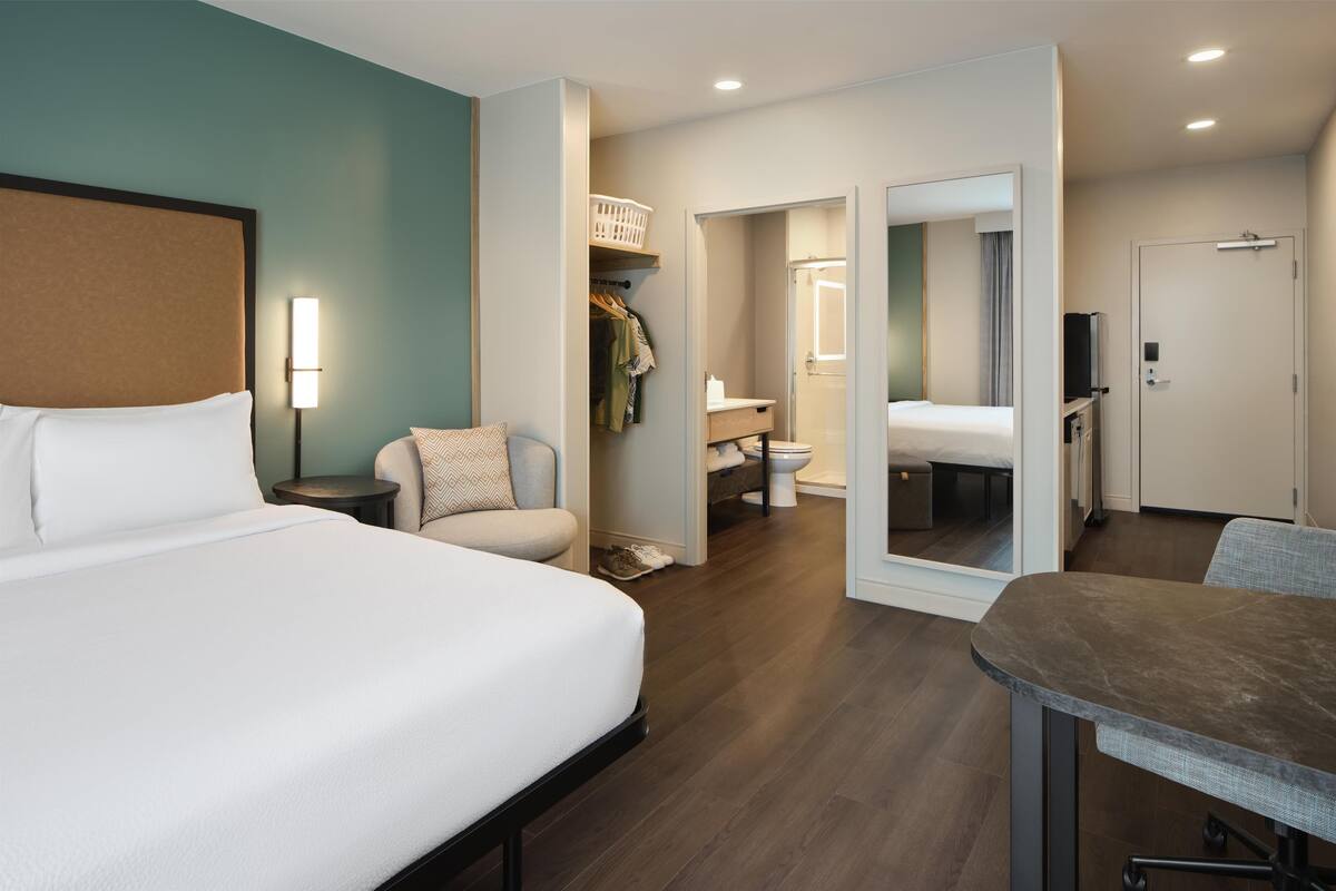 Una habitación de hotel con una cama grande, un escritorio, una silla, un armario y un baño.