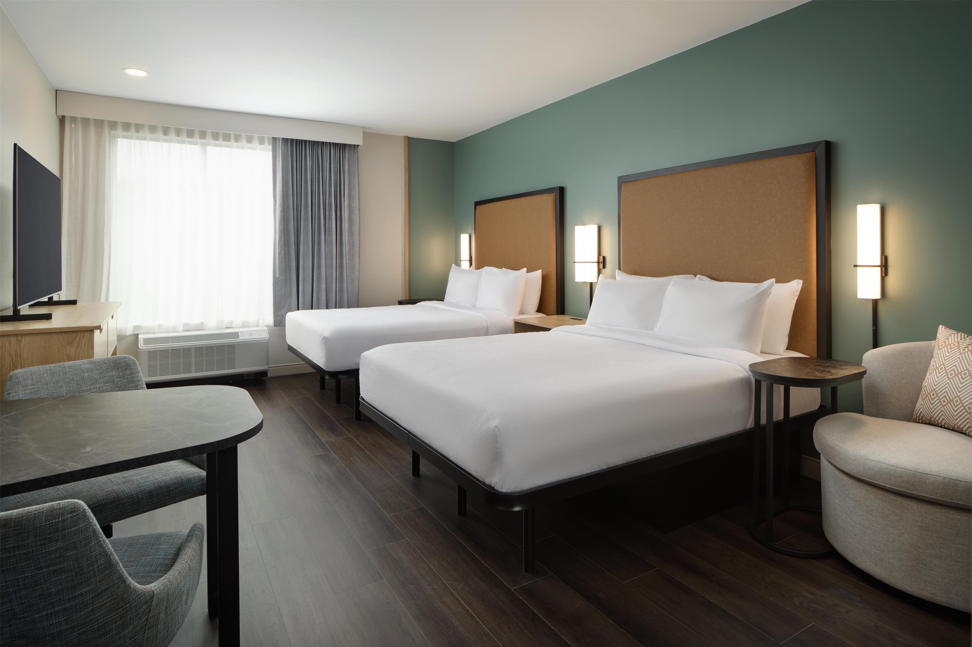Habitación de hotel con dos camas, televisión, mesa de comedor y sofá.