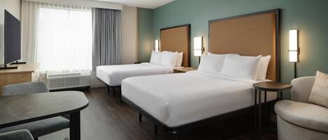 Habitación de hotel con dos camas, televisión, mesa de comedor y sofá.