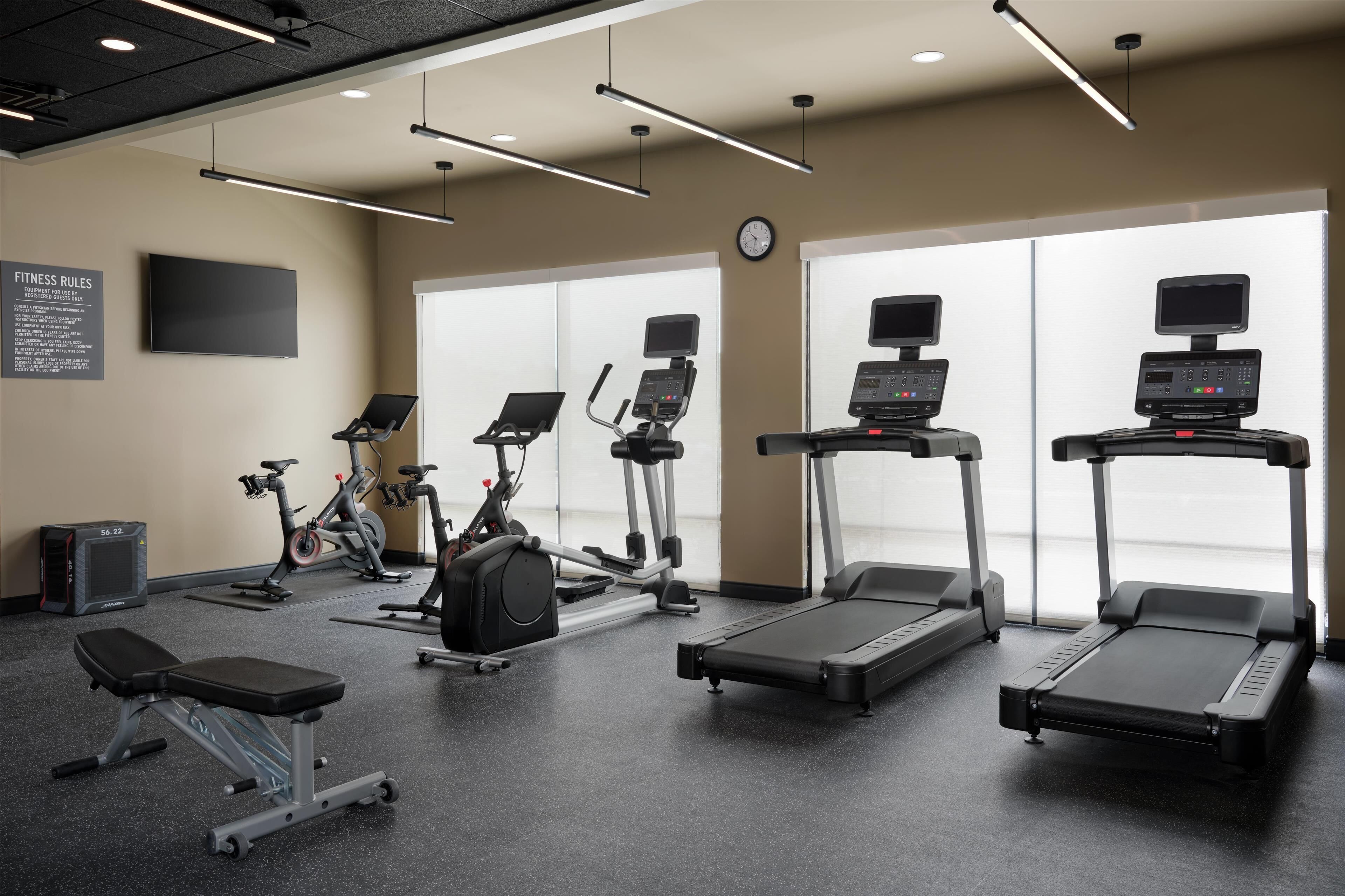 Une salle de sport équipée de tapis de course, de vélos elliptiques et d’un banc de musculation.