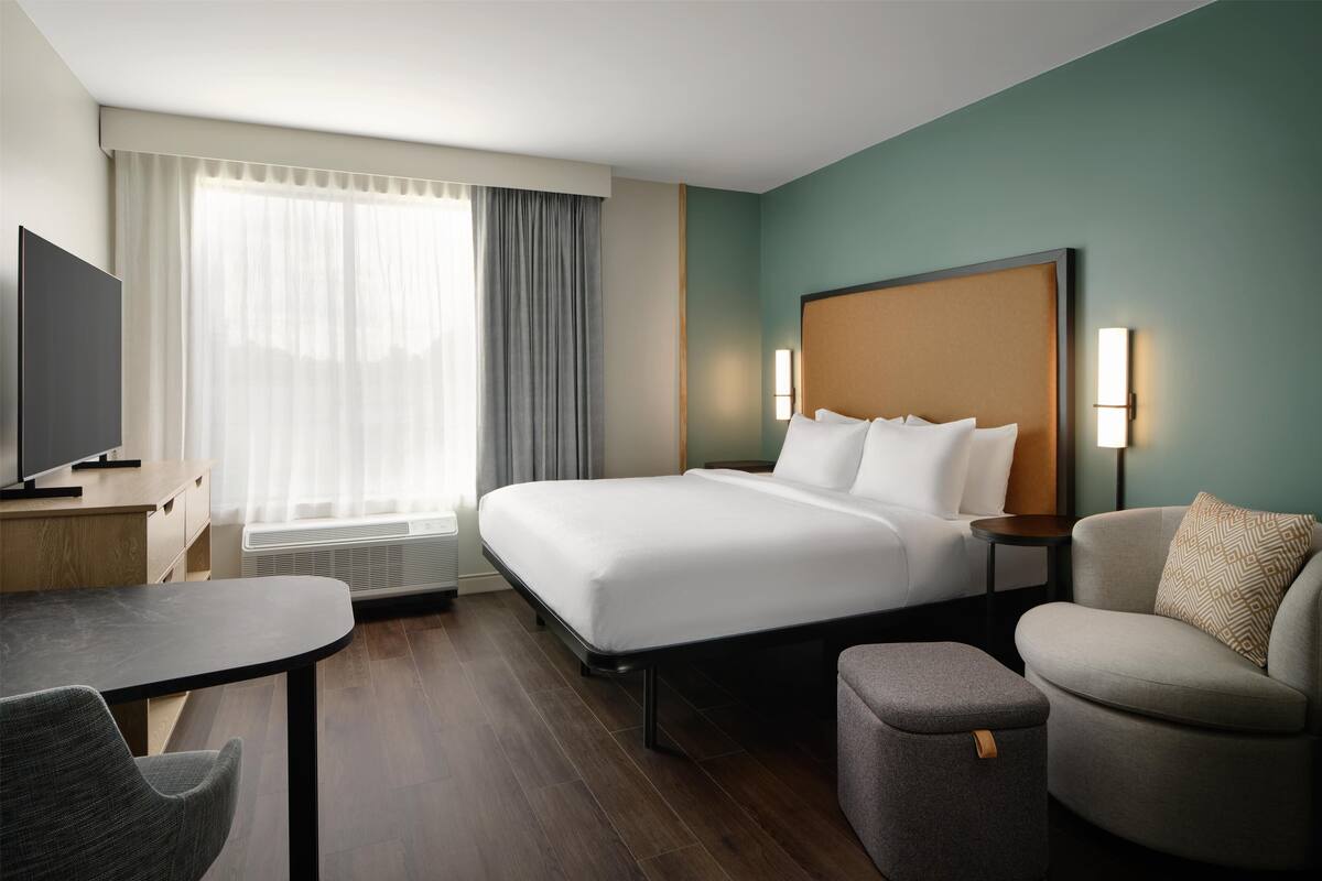 Una habitación de hotel con cama, escritorio, silla, sofá y televisor.