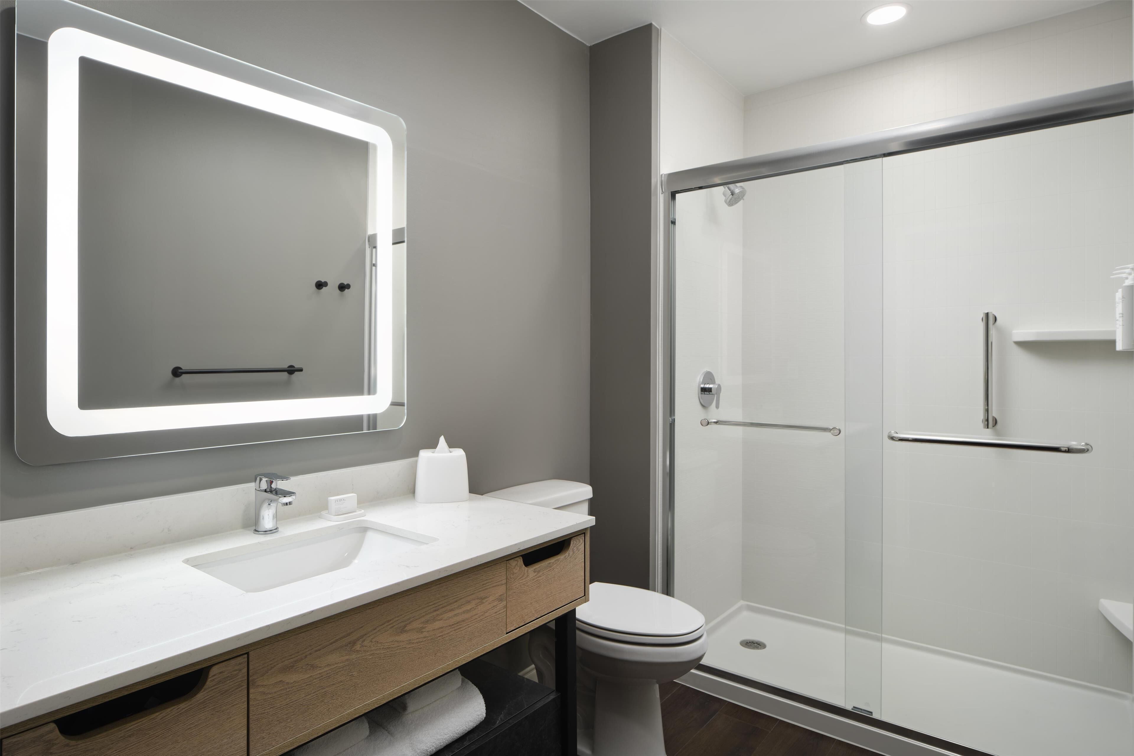 A modern bathroom with a large mirror, white sink, and a glass shower enclosure.
