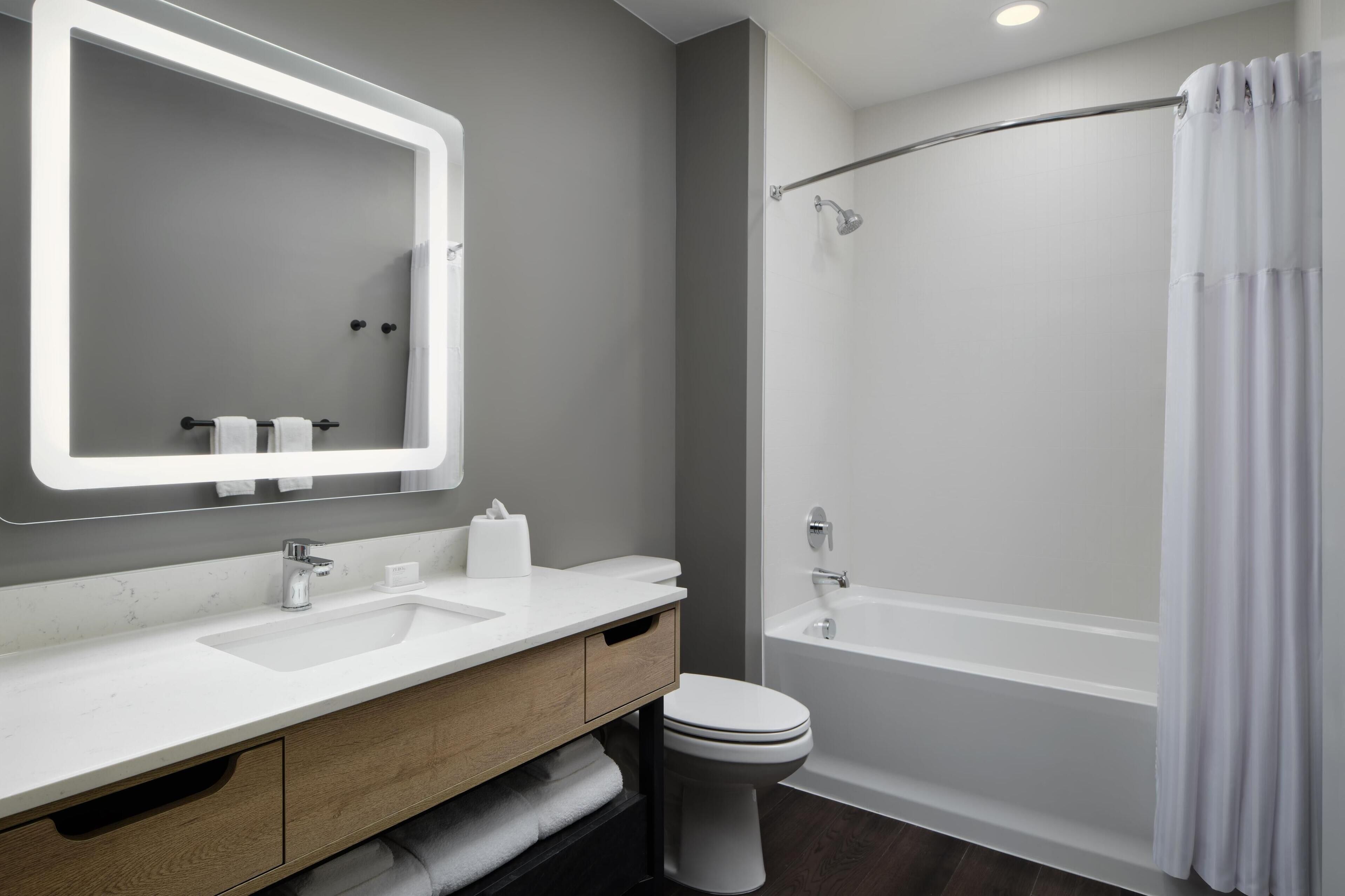 A modern bathroom with a white sink, mirror, and toilet, a bathtub, and a shower curtain.