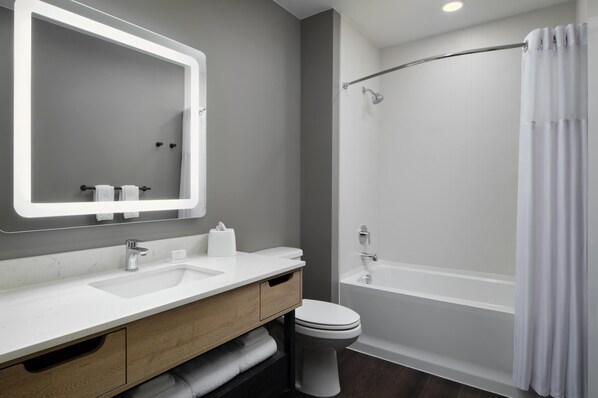 A modern bathroom with a white sink, mirror, and toilet, a bathtub, and a shower curtain.