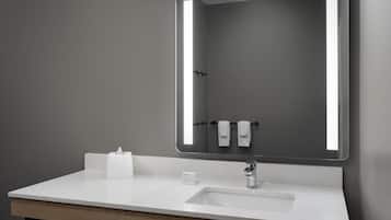 Un baño moderno con lavamanos blanco, espejo con luces LED y un perchero para toallas.