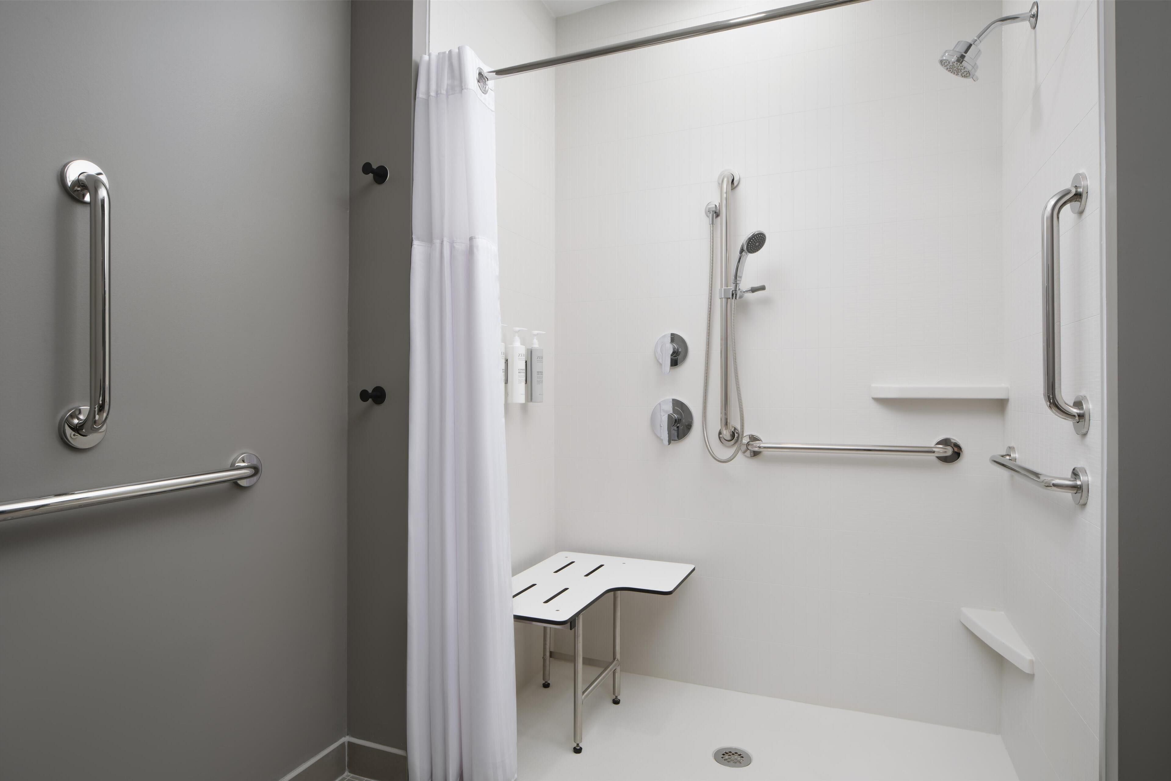 Un baño moderno con cabina de ducha, barras de apoyo y una mesita.