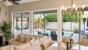 A spacious living room with a large sofa, a dining table, and a view of an outdoor pool area. - Luxe Retreat- Private Pool -BBQ- Peaceful Retreat- Comfort-Relax-Prime Location (Mesa)