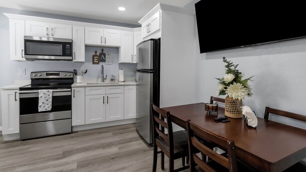 A modern kitchen with white cabinets, stainless steel appliances, and a dining area with a wooden table and chairs.