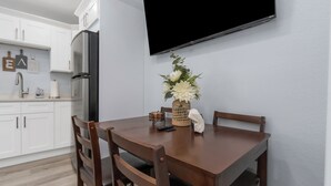 A modern kitchen with white cabinets, a black refrigerator, and a flat-screen TV mounted on the wall.