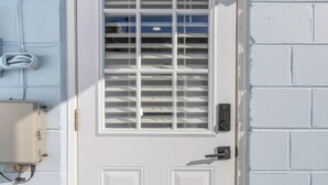 A white door with a window, a keypad lock, and a wall-mounted intercom.