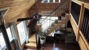A wooden cabin interior with a central staircase, a wood stove, and multiple clocks on the walls. - Charming loft cabin just 7 minutes from downtown (Talkeetna)